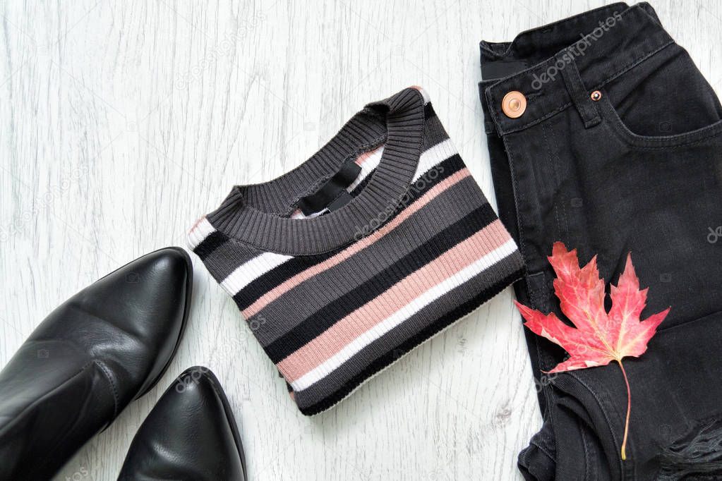 Striped sweater, black jeans, boots and red maple leaf. Fashionable concept