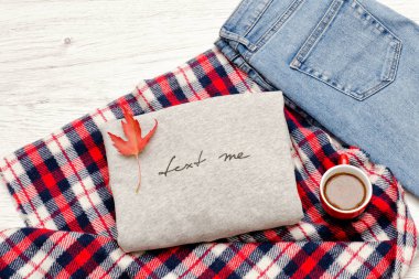 Gri kazak bir yazıt, ekose, kot pantolon, kahve kupa ve sonbahar yaprakları ile. Moda kavramı