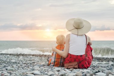 Anne ve oğlu okyanus kıyısında oturuyor. Arkadan görüntülemek