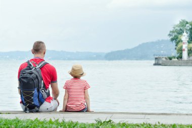 Baba ve oğul deniz arka plan, deniz feneri ve dağlar uzakta iskelede oturup. Arkadan Görünüm