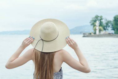 İskelede şapkalı kız. Dağlar ve deniz feneri arka planda. Arkadan görüntülemek