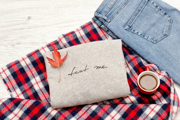 Gri kazak bir yazıt, ekose, kot pantolon, kahve kupa ve sonbahar yaprakları ile. Moda kavramı