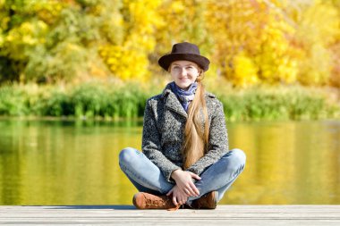 Şapkanı ve Paltonu iskelede oturan kız. Sonbahar, güneşli.