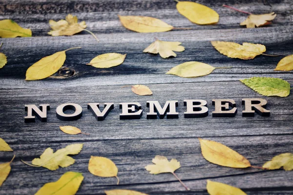Mot de novembre, lettres en bois. Cadre de feuilles jaunes, fond en bois — Photo
