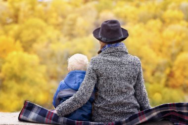 Anne ve oğlu bir yüksek yerde oturuyorsun. Sonbahar. Mesafe ormanda. Arkadan Görünüm