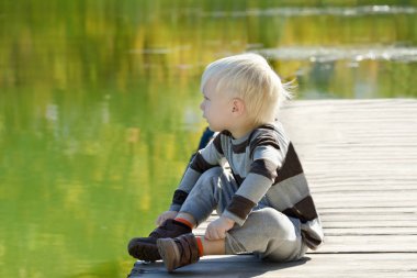 Sarışın çocuk iskelede oturuyordu. Sonbahar, güneşli bir gün.
