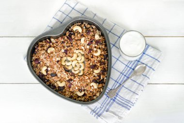 Granola bir kalp şeklinde fırın tepsisine, bir bardak yoğurt içinde. Beyaz arka plan. Gıda kavramı