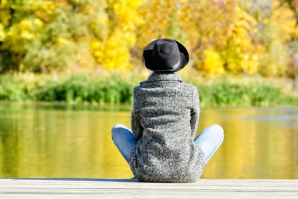 모자와 코트 dock에 앉아 있는 소녀. 가 햇살. 후면 모습 — 스톡 사진