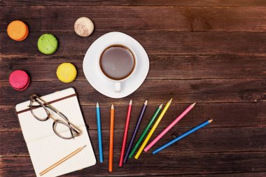 Kahve kupa, bademli kurabiye, renkli kalemler ve ahşap bir zemin üzerine gözlük ile not etmek