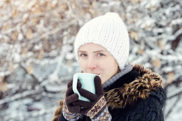 Piękna dziewczyna w białym kapeluszu, rękawiczkach i z kubkiem herbaty, biały śnieżny tło — Zdjęcie stockowe