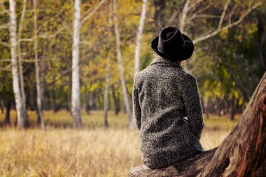 Bir günlük sonbahar ormanın içinde oturan şapkalı kız. Arkadan Görünüm.