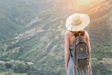 Bir sırt çantası ve bir şapka duran yeşil dağların bir arka plan ile güzel kız