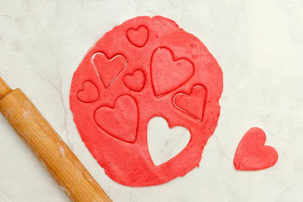 Bir oklava ve beyaz bir tablo kalpleri dışarı kesim ile kırmızı hamur — Stok fotoğraf