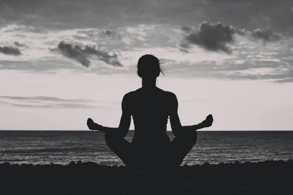 Woman meditating on the beach in lotus position. Silhouette, black and white — Stock Photo, Image