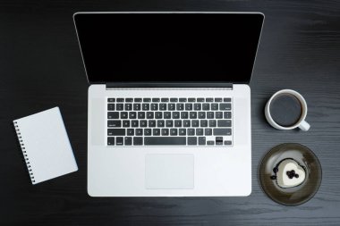 Bir fincan kahve, not defteri ve tatlı bir siyah arka plan üzerine açık gümüş dizüstü bilgisayar