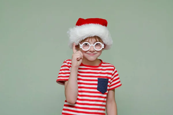 Pojke i tomtens hatt och glasögon håller hans pekfinger upp — Stockfoto