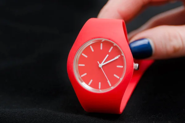 Relógio vermelho em uma mão feminina sobre um fundo preto. Close-up — Fotografia de Stock