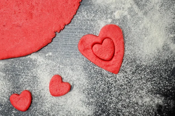 Красное тесто с вырезанными сердцами и мукой на черном столе — стоковое фото