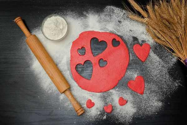 Masa roja con corazones cortados y harina en la mesa negra . — Foto de Stock