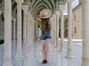 Sütunlar arasında bir sırt çantası konumu olan şapkalı kız. Arkadan Görünüm