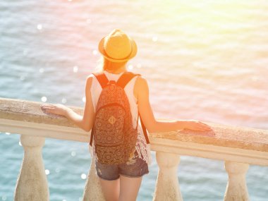 Balkonda duran ve denize bakarak şapkalı kız