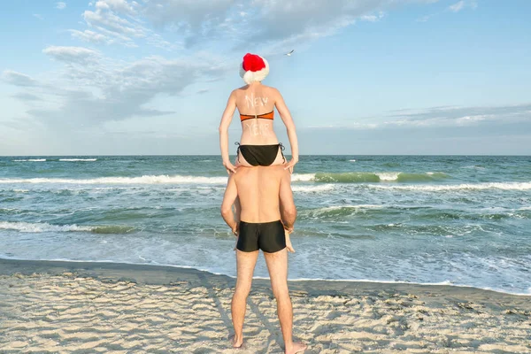 Mädchen mit Weihnachtsmütze sitzt auf den Schultern eines Mannes. Meeresküste — Stockfoto