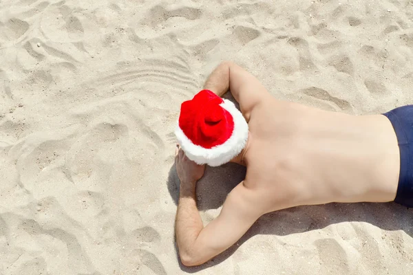 Mann mit Weihnachtsmannmütze auf dem Sand liegend. Ansicht von oben — Stockfoto