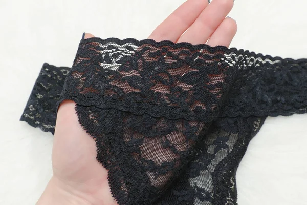 Black lace underwear in a female hand on a white fur