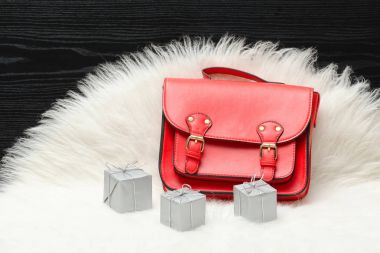 Kırmızı çanta ve mini hediye kutusu beyaz kürk üzerinde. Moda kavramı