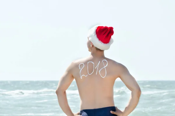 Der Mann mit dem Weihnachtsmannhut steht am Ufer des Meeres. Anmeldung 2018 — Stockfoto