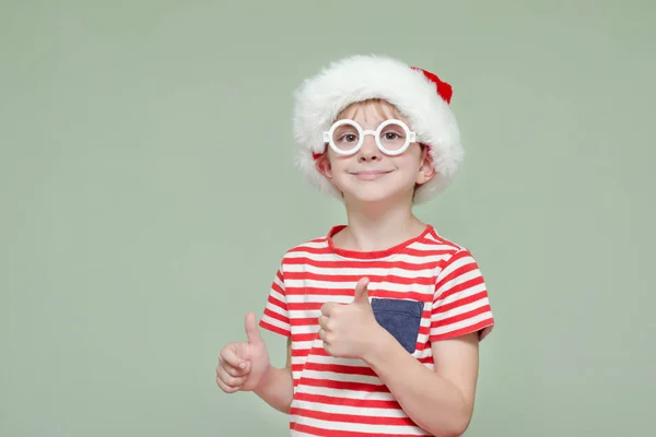 Chłopiec w Santa kapelusz i okulary, uśmiechając się i pokazuje kciuk w — Zdjęcie stockowe