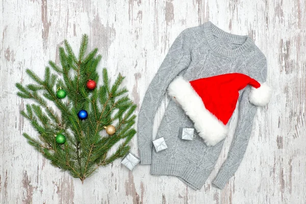O chapéu do Pai Natal numa camisola cinzenta. Ramo de abeto decorado. Costas de madeira — Fotografia de Stock