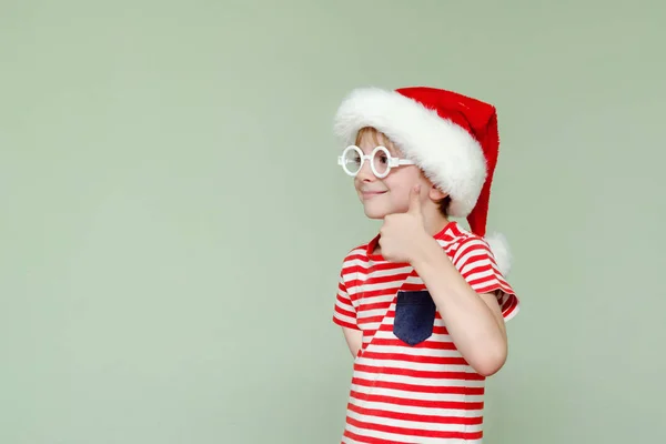 Chłopiec w santa kapelusz i okulary pokazuje kciuk w — Zdjęcie stockowe