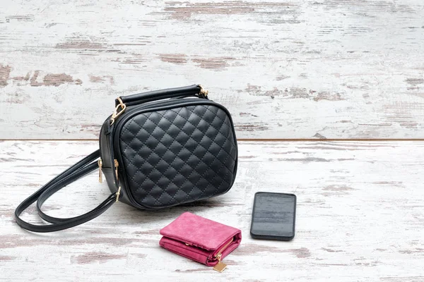 Маленькая черная женская сумочка, розовый кошелек и смартфон на деревянном фоне — стоковое фото