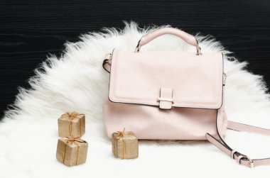 Beyaz kürk, siyah masada pembe çanta ve hediye kutusu