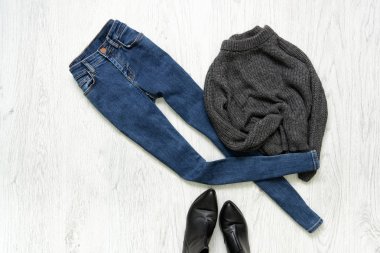 Mavi jeans, gri kazak ve ahşap arka plan üzerinde siyah ayakkabı