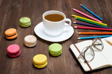 Kahve kupa, bademli kurabiye, renkli kalemler ve gözlüklü bir not defteri