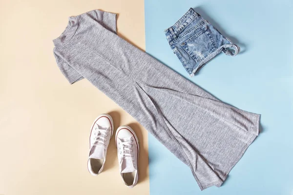 Modisches Konzept. Frauen im urbanen Stil. graues Kleid, weiße Turnschuhe und Jeans auf blauem Hintergrund, beige — Stockfoto