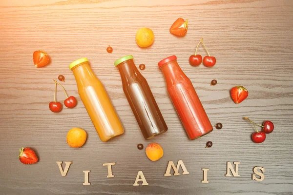 Three bottles with juice, fruit and inscription vitamins on a black wooden background, food concept