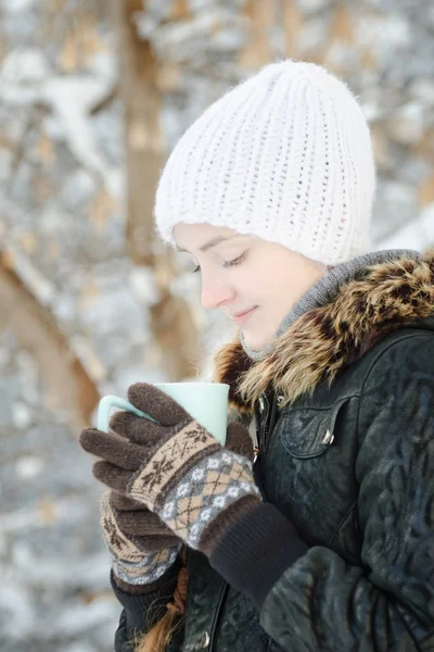 Dziewczyna w białym kapeluszu wygląd w filiżankę herbaty. Zima, na zewnątrz — Zdjęcie stockowe