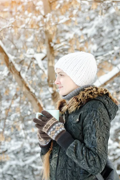 一个戴着白帽子的女孩喝了杯茶。冬天, 户外。侧面视图 — 图库照片