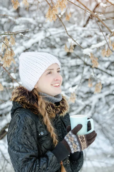 Chica sonriente con un sombrero blanco con una taza de té. Invierno, al aire libre — Foto de Stock
