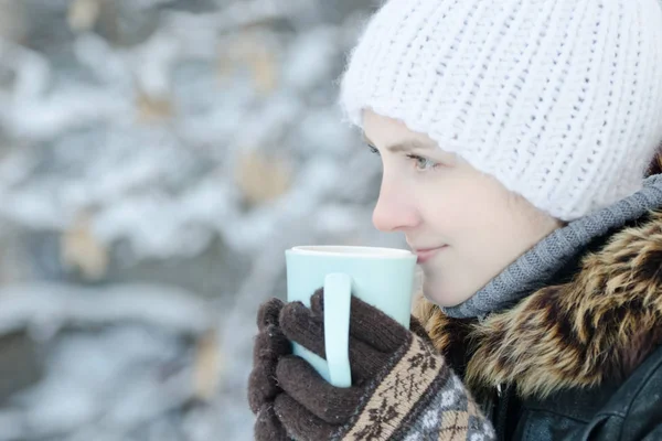 Дівчина в зимовому одязі п'є чай з чашки. Вид збоку — стокове фото