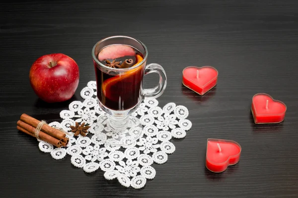 Ζεστό κρασί με μπαχαρικά. Κεριά σε σχήμα καρδιά, ραβδιά κανέλας και μήλο. Μαύρο φόντο ξύλου — Φωτογραφία Αρχείου
