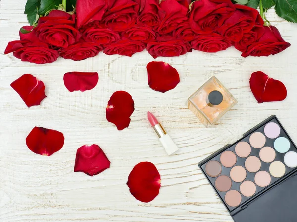 Bukiet czerwonych róż, perfumy, szminki i eyeshadow palette — Zdjęcie stockowe