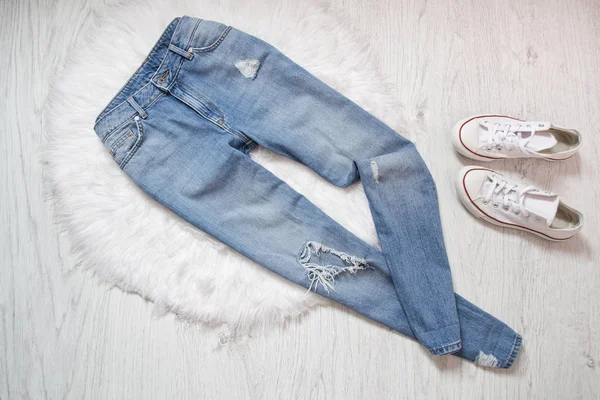 Blauwe ragged jeans en witte sneakers op wit bont. — Stockfoto