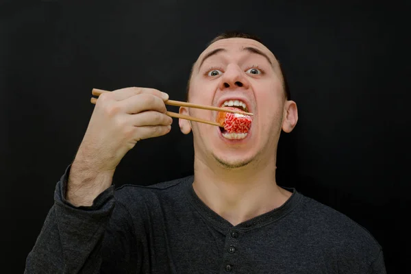 L'uomo affamato mangia rotoli con le bacchette. Bocca aperta — Foto Stock
