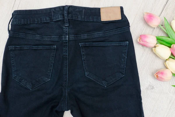 Fashion concept. Achterste gedeelte van de zwarte jeans en boeket tulpen. — Stockfoto