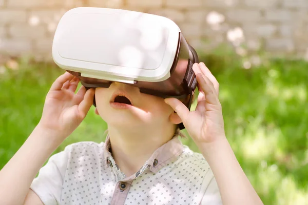 Niño en un casco de realidad virtual sobre un fondo de hierba verde —  Fotos de Stock