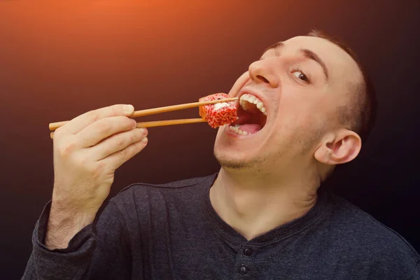 Ο άνθρωπος τρώει ρολά με chopsticks. Ανοιχτό το στόμα. Μαύρο φόντο — Φωτογραφία Αρχείου